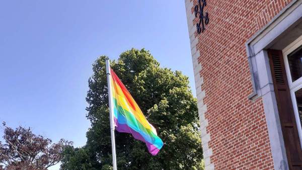 Een regenboogvlag aan een stok langs het gemeentehuis van Dilbeek