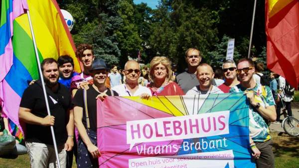 De groep vrijwilligers van het Holebihuis in Riga tijdens de Pride-optocht. Ze dragen regenboogvlaggen, de Belgische vlag en een vlag van het Holebihuis en kijken naar de camera.