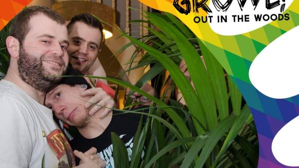 Een foto van enkele personen die poseren voor de camera, drie personen links zijn goed zichtbaar en achter enkele groene planten rechts van hen lijken nog enkele mensen te staan. Over de foto is er een regenboog-graphic geplakt en in de rechterbovenhoek leest er 'GROWL! OUT IN THE WOODS' in zwarte letters.